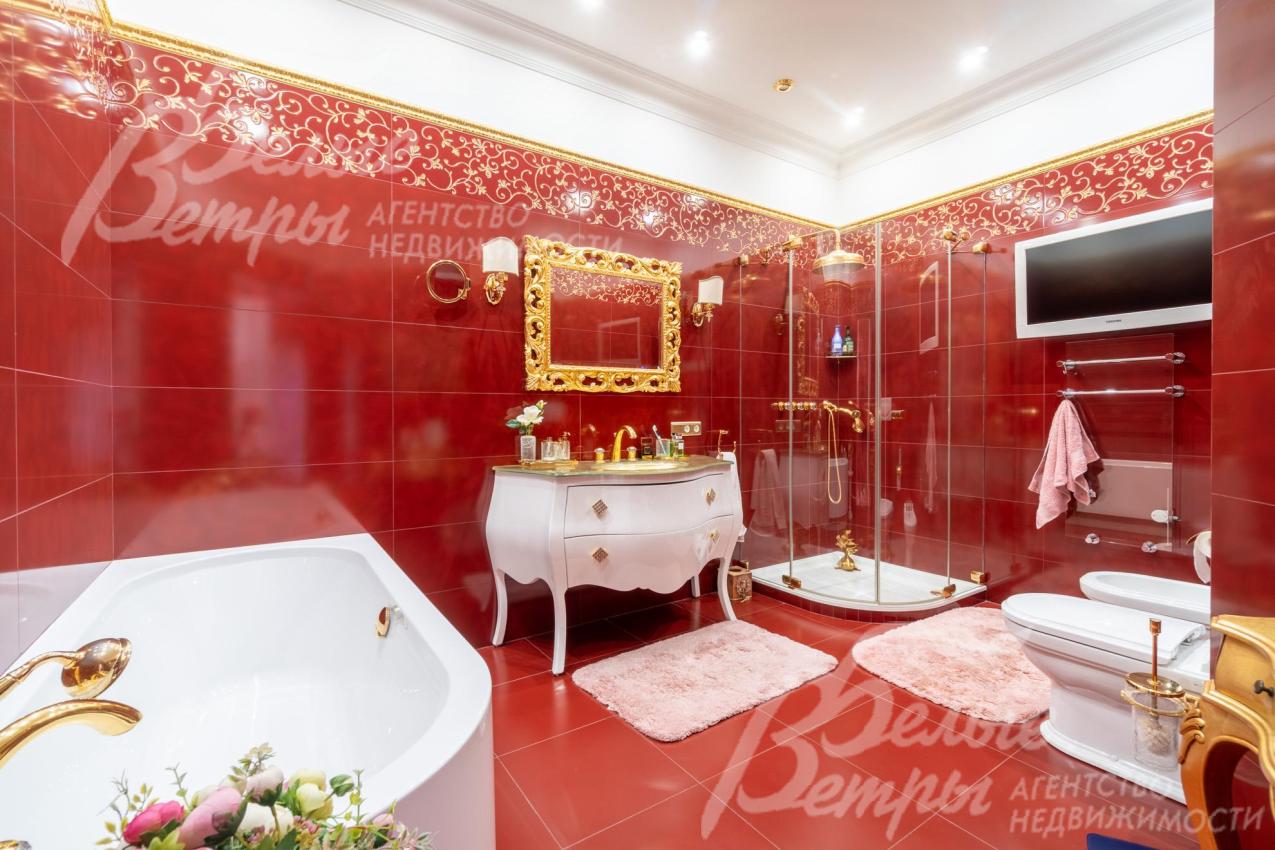 Санузел оформлен в цветовой гамме с доминированием глубокого красно-кирпичного оттенки, над раковиной - большое зеркало в массивной золотой раме с орнаментом