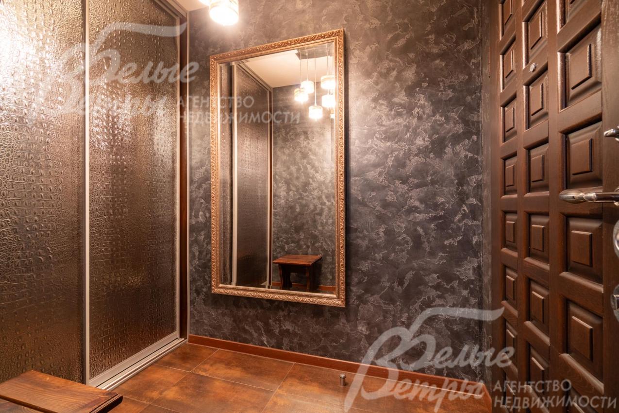 В прихожей находится большое зеркало в багетной раме с латунным оттенком и шкаф-купе с дверцами, украшенными текстурным рисунком