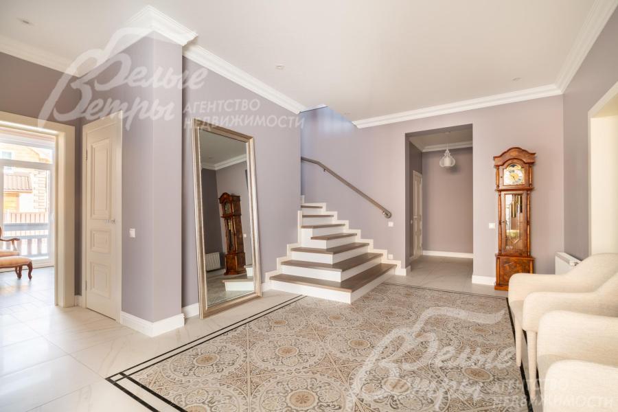 Интерьер холла в светлых тонах дополняют удобные кресла и элегантные напольные часы в классическом стиле