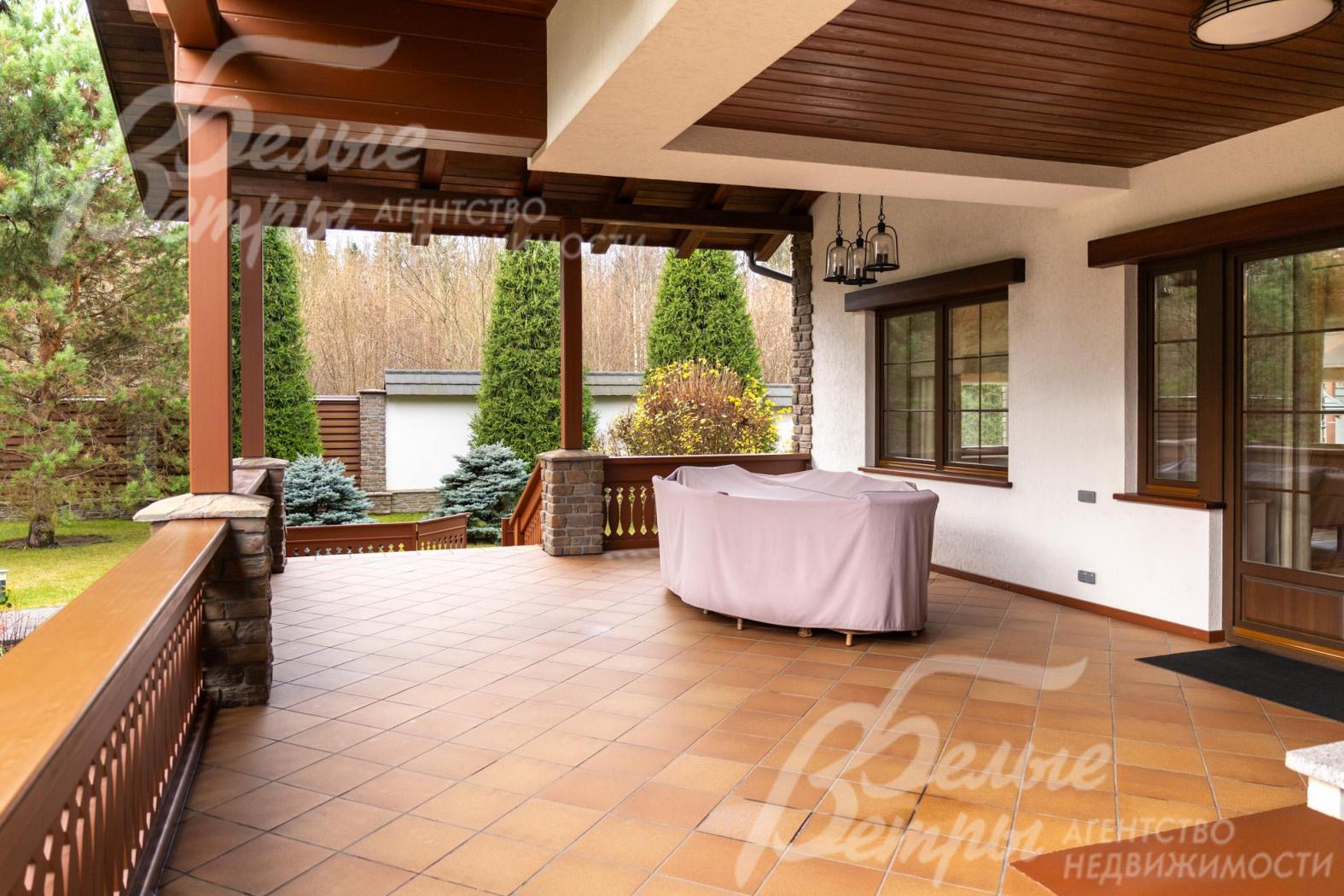 Одна из террас с плиточным покрытием тёплого терракотового оттенка, обрамлённая деревянными перилами и колоннами