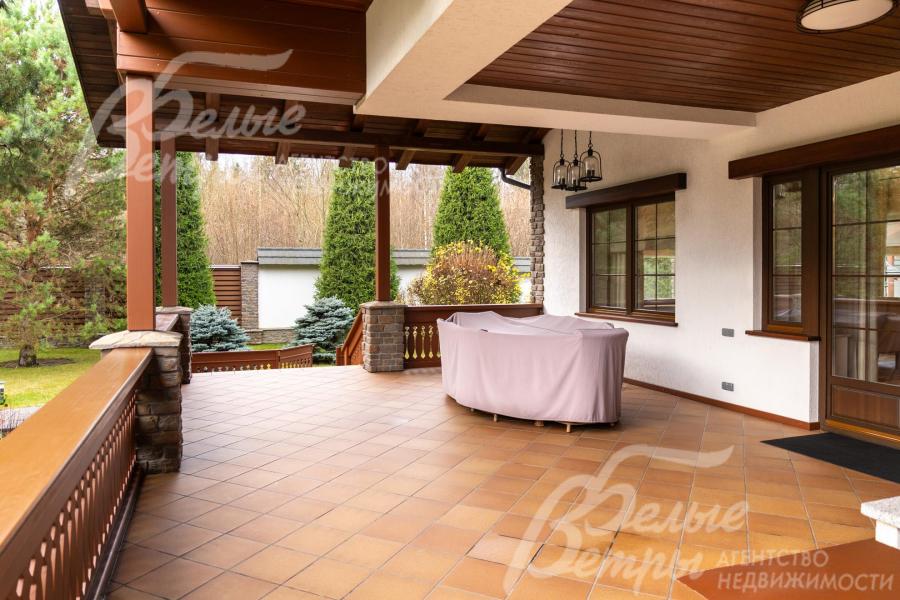 Одна из террас с плиточным покрытием тёплого терракотового оттенка, обрамлённая деревянными перилами и колоннами