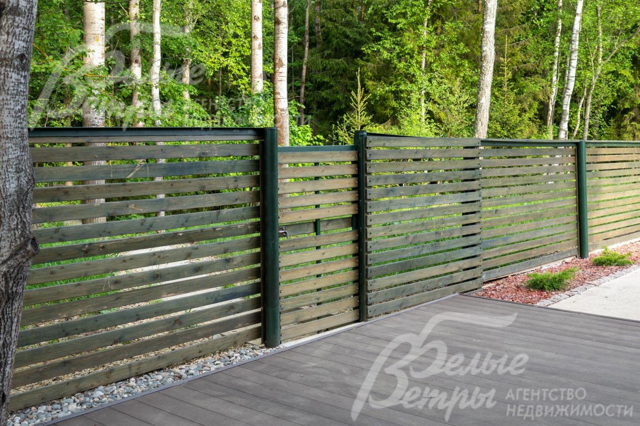 Участок огорожен деревянным забором на металлических столбах высотой 2,2 м