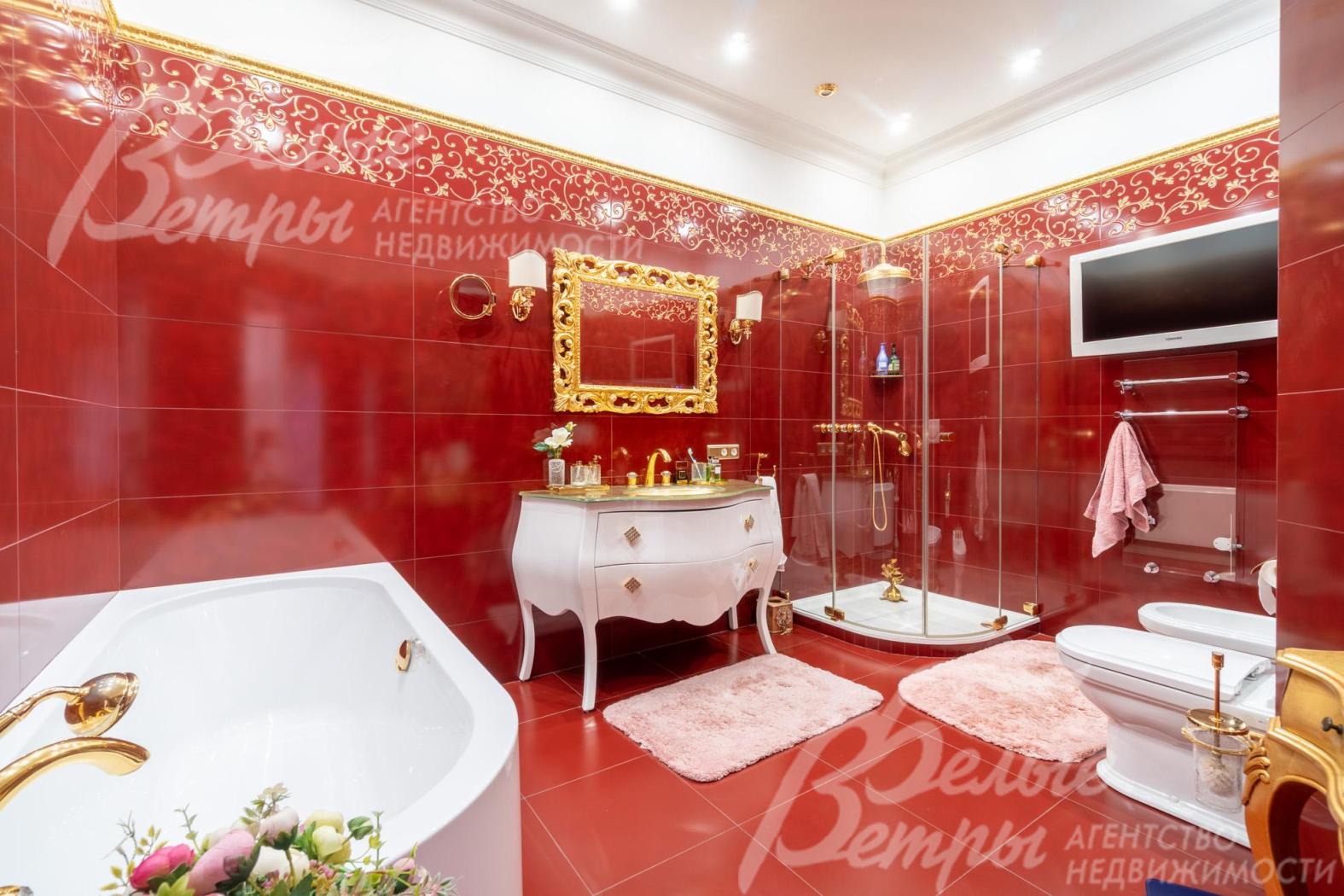 Санузел оформлен в цветовой гамме с доминированием глубокого красно-кирпичного оттенки, над раковиной - большое зеркало в массивной золотой раме с орнаментом