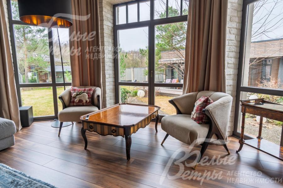 Гостиная - с эркером, оформленными окнами от пола до потолка, где создана зона отдыха. Большие окна наполняют комнату естественным светом и открывают вид на участок