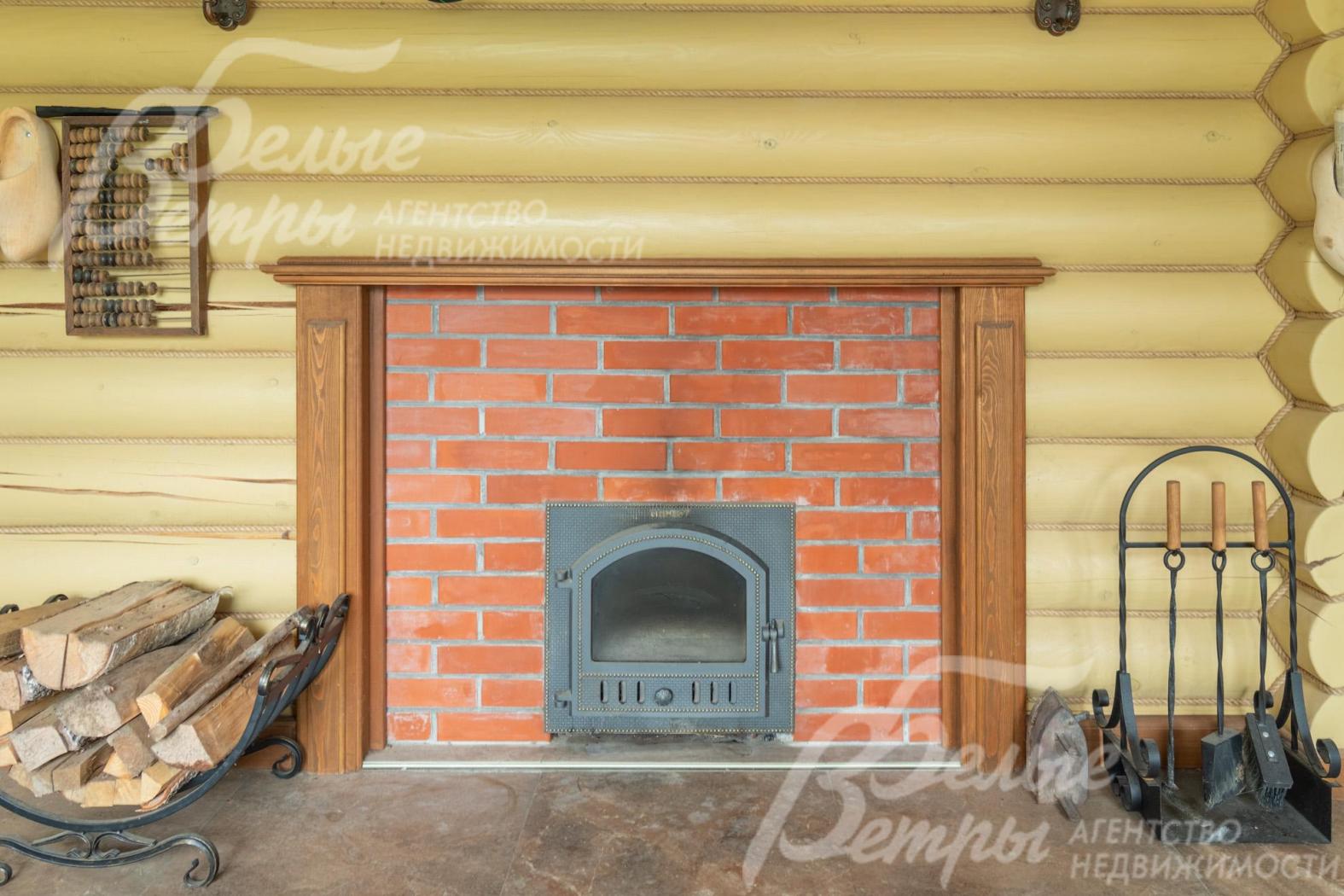 Печь в кирпичной кладке, рядом - дровница и каминный набор