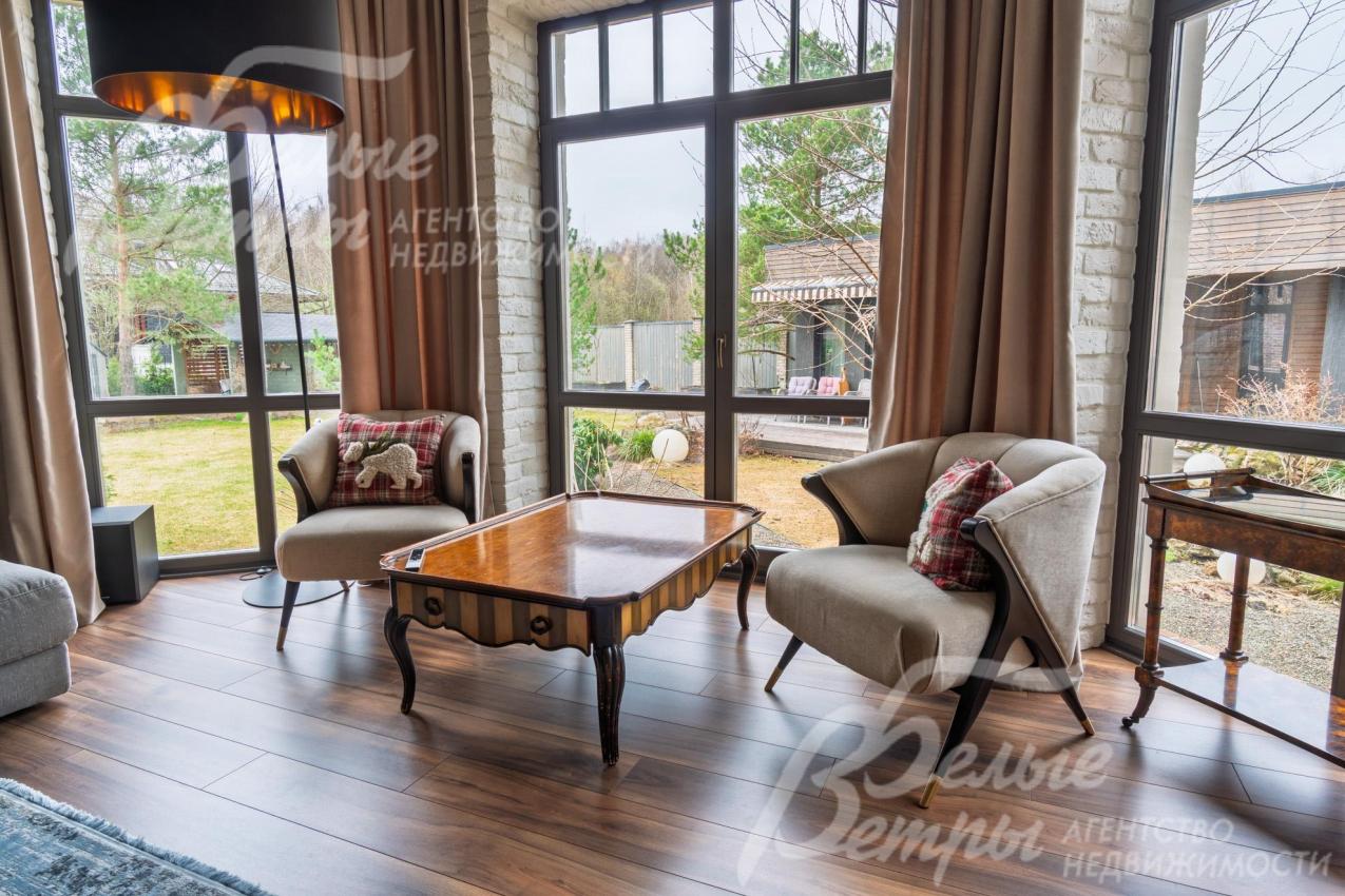 Гостиная - с эркером, оформленными окнами от пола до потолка, где создана зона отдыха. Большие окна наполняют комнату естественным светом и открывают вид на участок