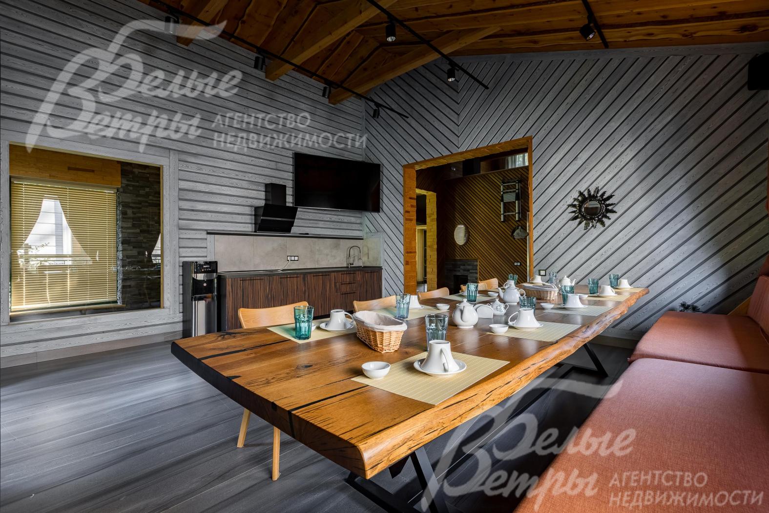 Интерьер кухни-гостиной бани выполнен в стиле лофт с элементами рустикального дизайна. В центре - массивный обеденный стол из натурального дерева с необработанными краями