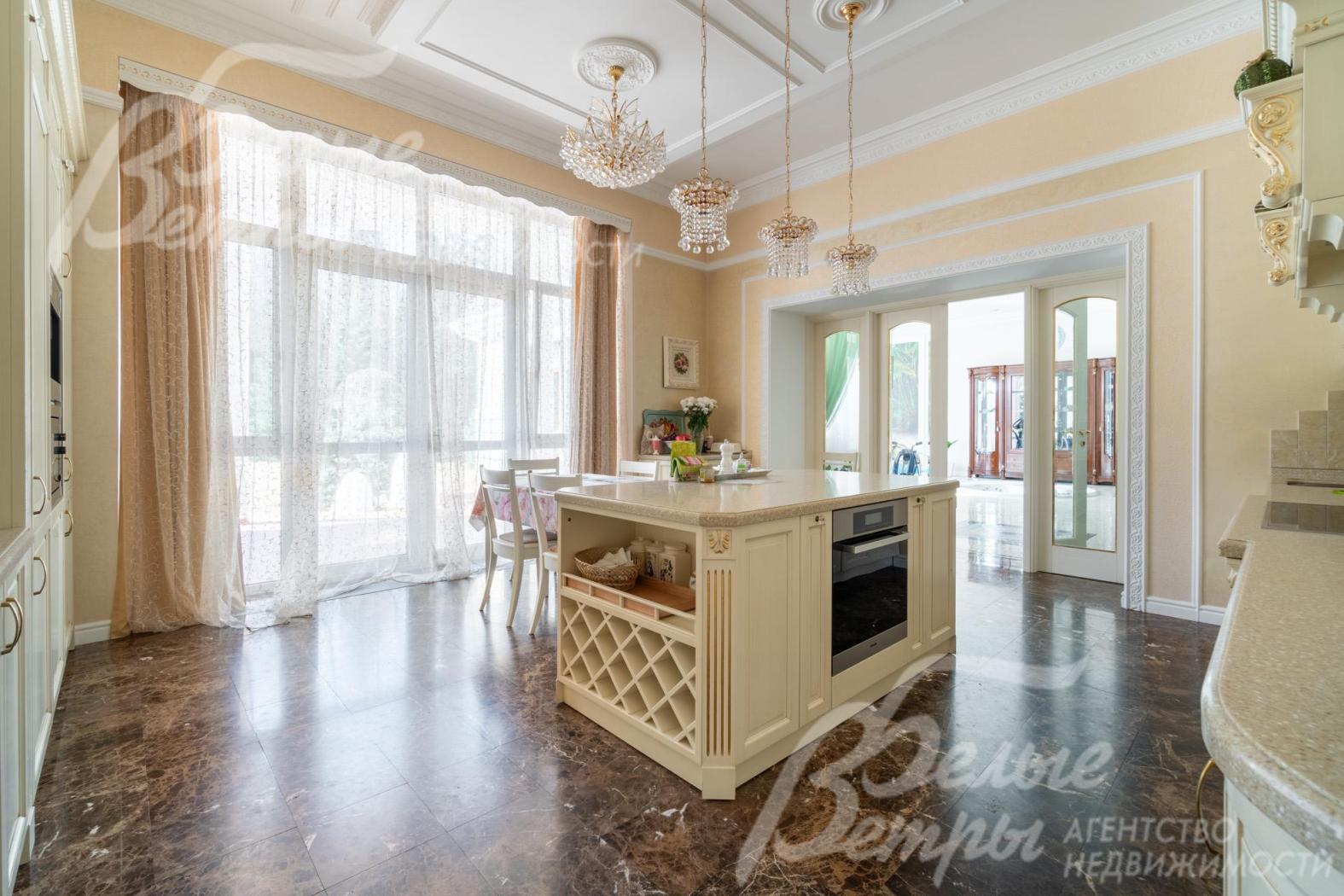 На кухне - итальянский гарнитур из массива дерева с фигурными карнизами, филёнчатыми фасадами, колоннами, позолотой. Из кухни есть выход на просторную террасу через стеклянный портал