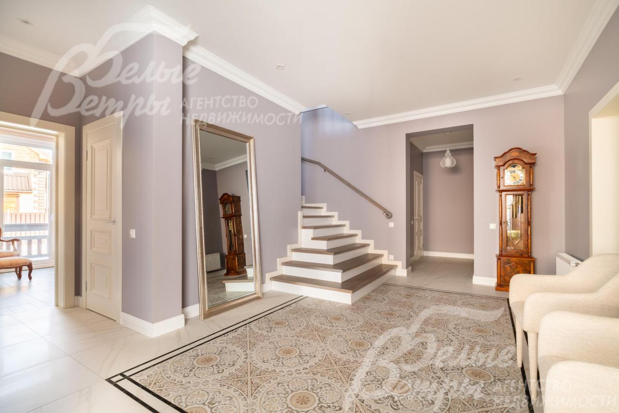 Интерьер холла в светлых тонах дополняют удобные кресла и элегантные напольные часы в классическом стиле