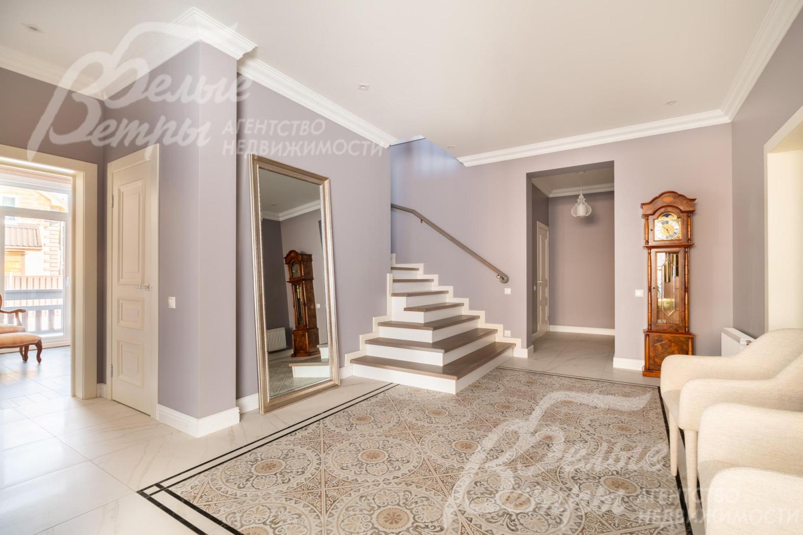 Интерьер холла в светлых тонах дополняют удобные кресла и элегантные напольные часы в классическом стиле