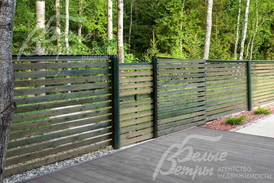 Участок огорожен деревянным забором на металлических столбах высотой 2,2 м